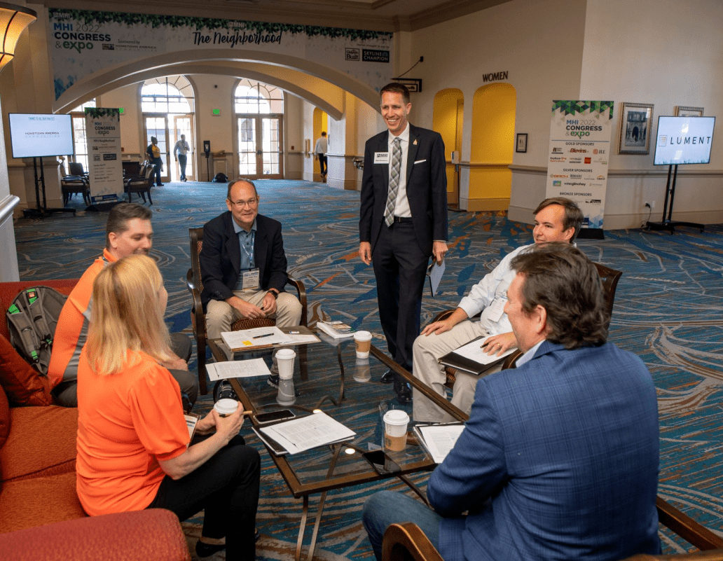 6 Meeting Attendees Laugh Around Low Table On Chairs and Couches