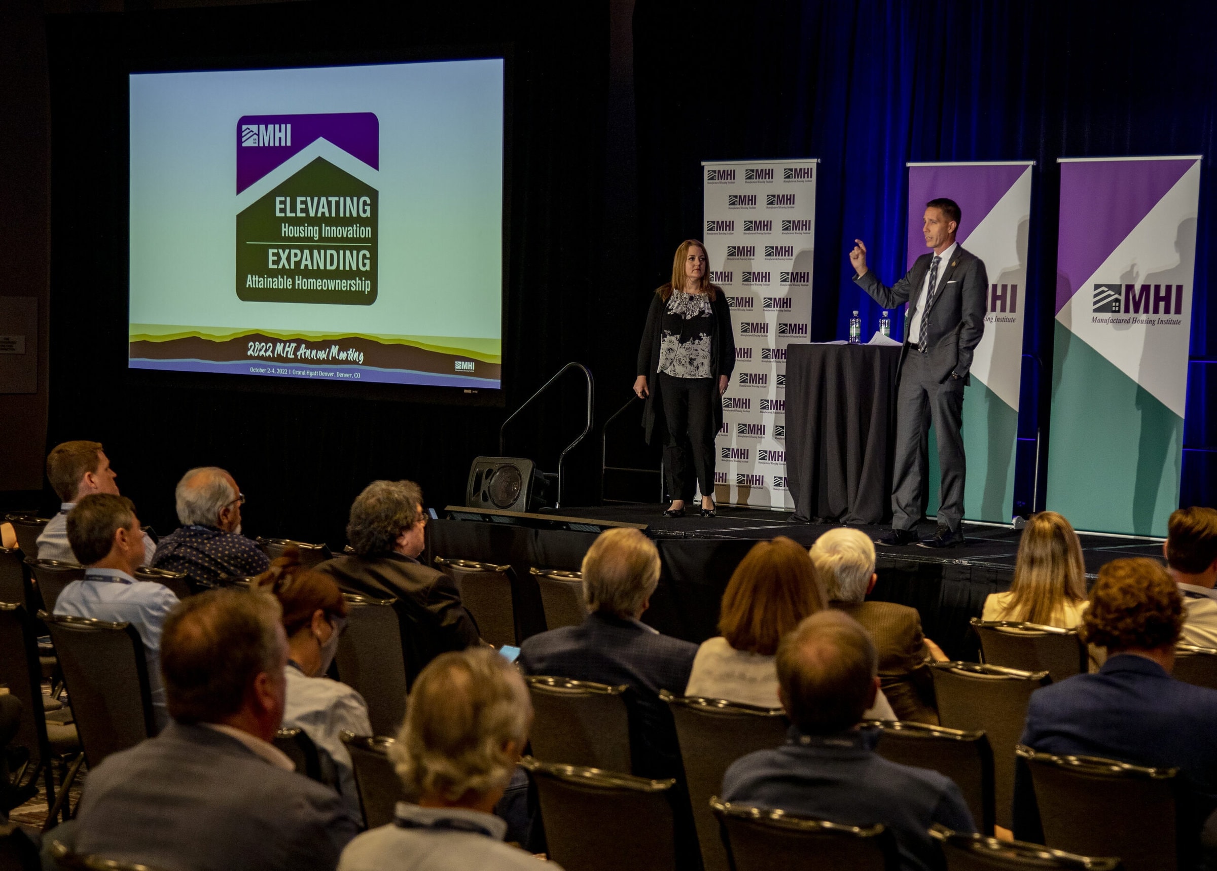 Man and woman in business attire on stage presenting to audience