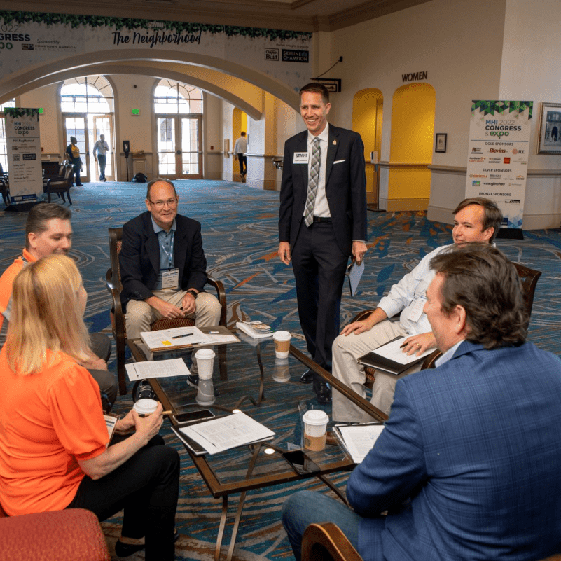 6 Meeting Attendees Laugh Around Low Table On Chairs and Couches