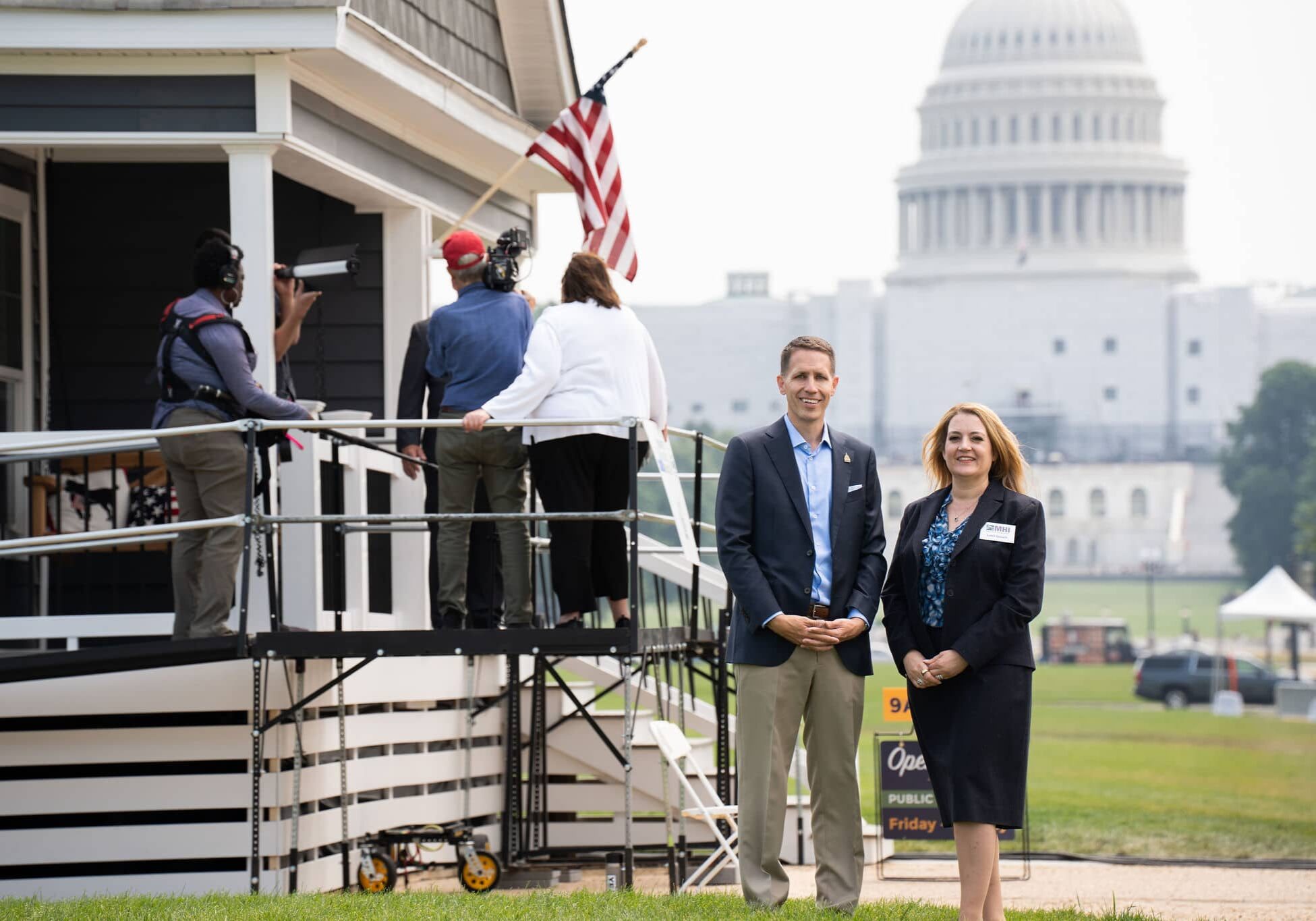 Two people in business attire beside manufactured home in front of the capitol