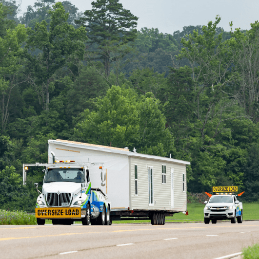 White truck carying a cream home followed by two trucks with Oversized Load signs